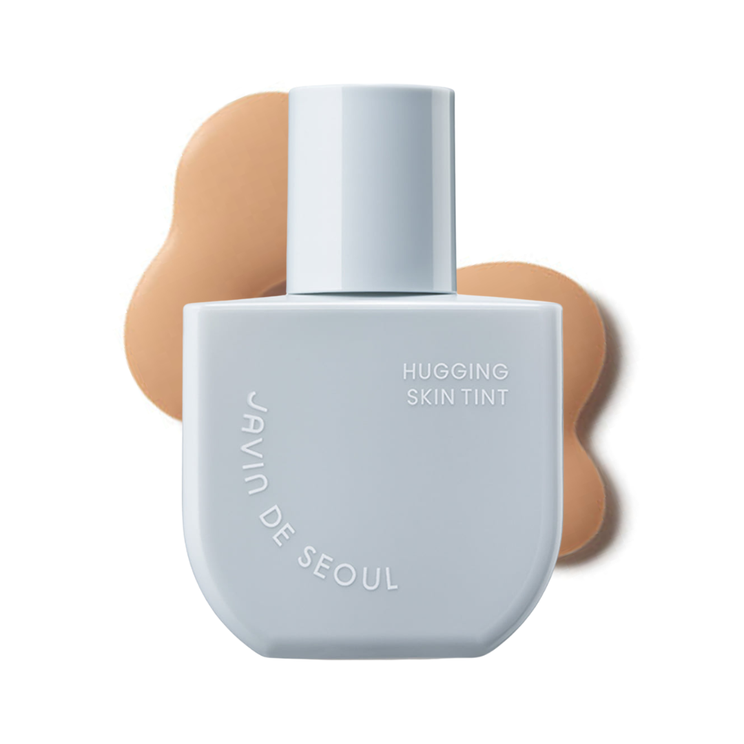 Lys grå flaske med "Hugging Skin Tint", brun farveprøve bagved.