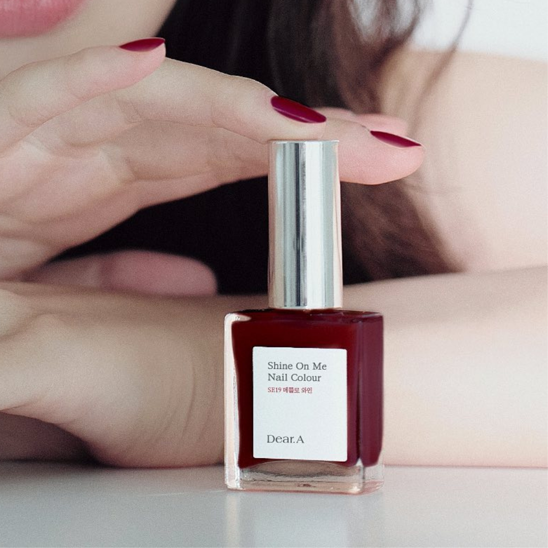 Rød neglelakflaske "Shine On Me" med matchende manicurerede negle over flasken.