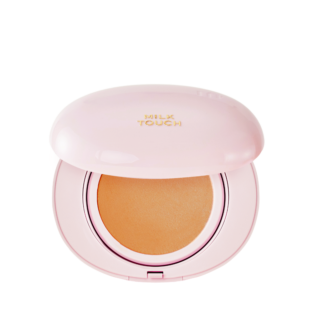 Pink kompakt med guldtekst "Milk Touch" og beige pude indeni.