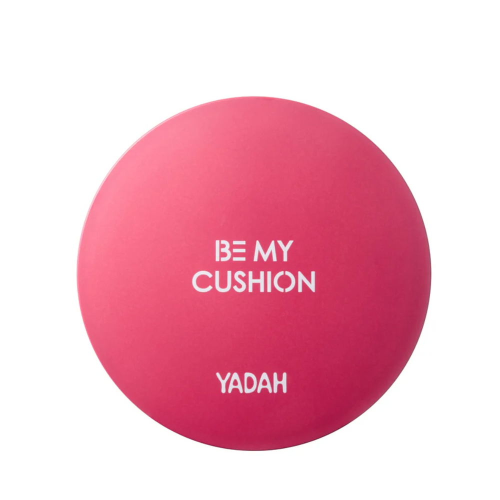 Rundt, lyserødt pudderdåse med hvid tekst "BE MY CUSHION" og "YADAH".