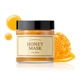 Glas med "Honey Mask" fra I'm From, sort låg, beige etiket, og honningkage i baggrunden.